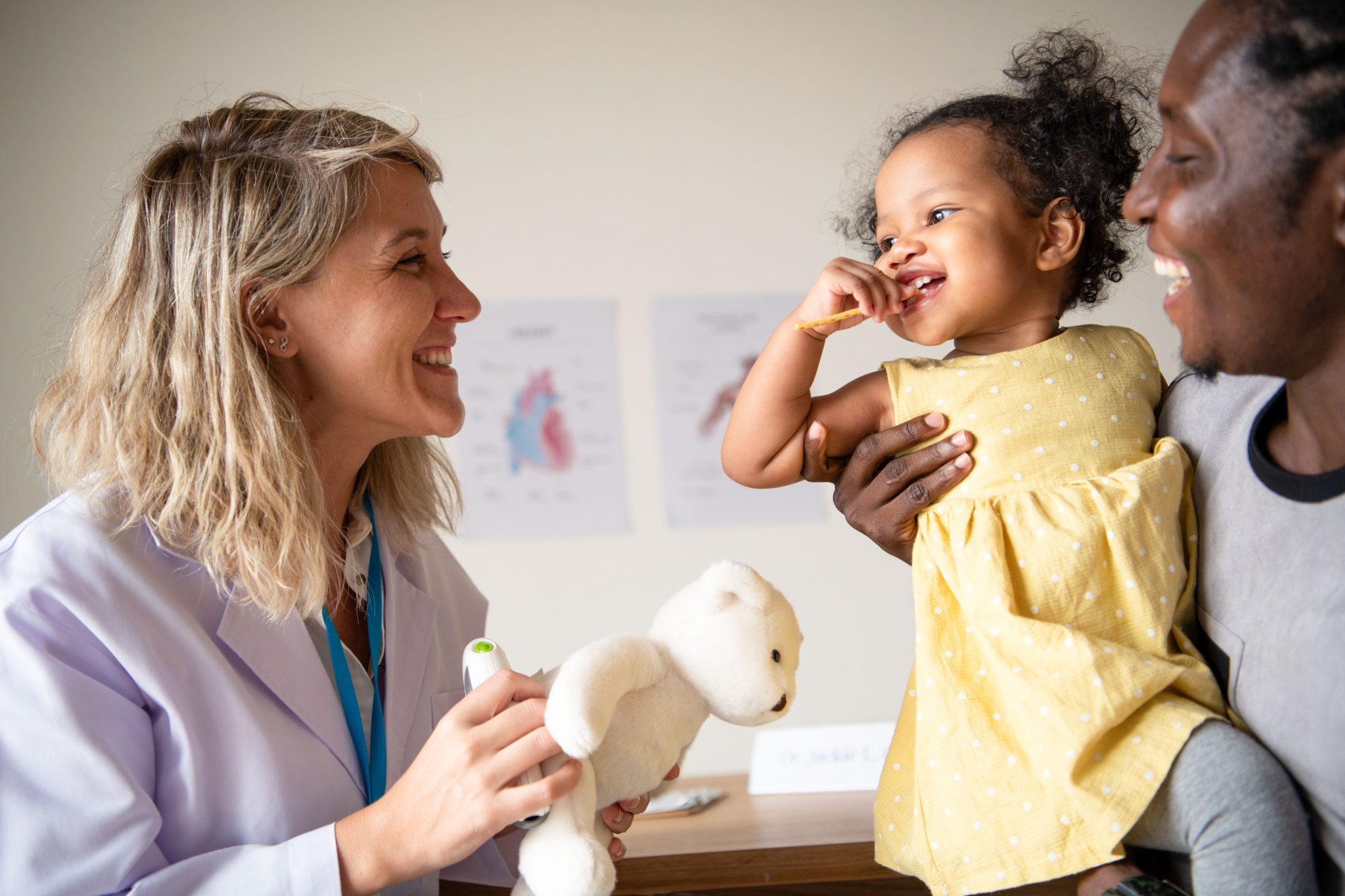 a female doctor holding a teddy bear of a young girl at the doctors