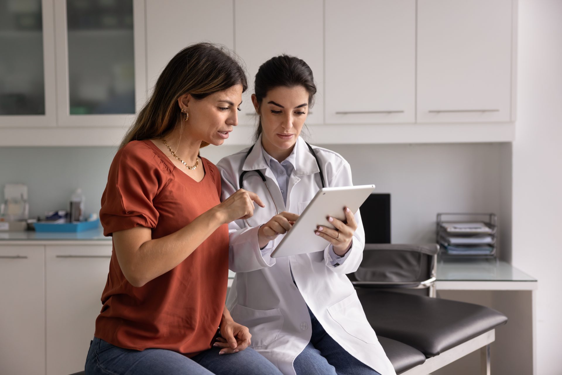 a female doctor looking at an ipad with a female patient
